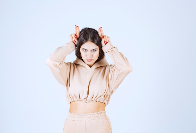 Foto gratuita mujer joven en una sudadera con capucha rosa haciendo orejas de conejo