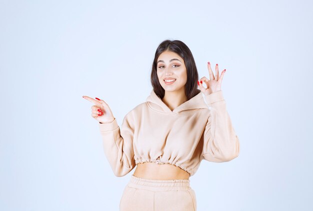 Mujer joven en una sudadera con capucha rosa mostrando buen signo de mano