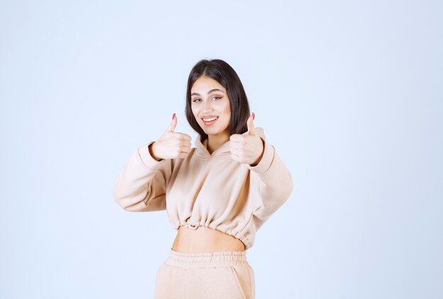 Mujer joven en una sudadera con capucha rosa mostrando buen signo de mano