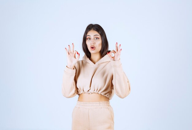 Mujer joven en una sudadera con capucha rosa que muestra el signo de la mano de satisfacción