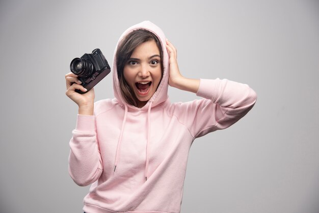 Mujer joven en sudadera sosteniendo la cámara felizmente.