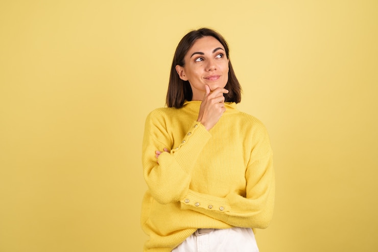 Foto gratuito mujer joven con suéter amarillo cálido tocando su barbilla