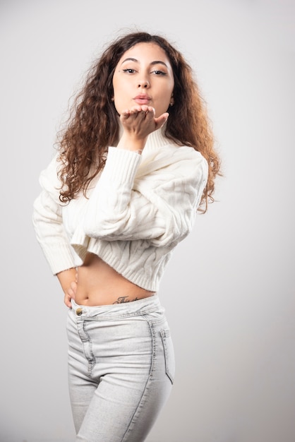 Foto gratuita mujer joven en suéter blanco de pie sobre una pared blanca. foto de alta calidad