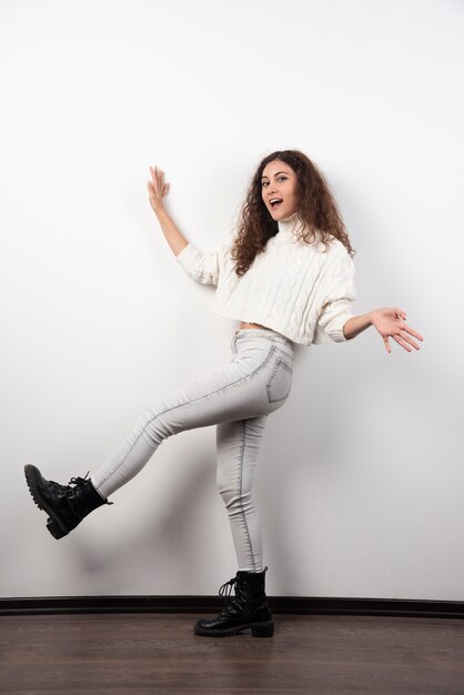 Mujer joven en suéter blanco de pie sobre una pared blanca. Foto de alta calidad