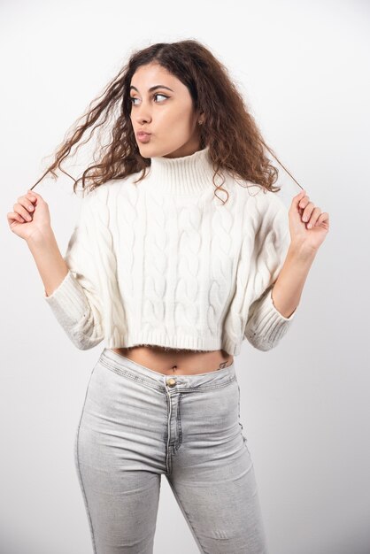 Mujer joven en suéter blanco de pie sobre una pared blanca. Foto de alta calidad