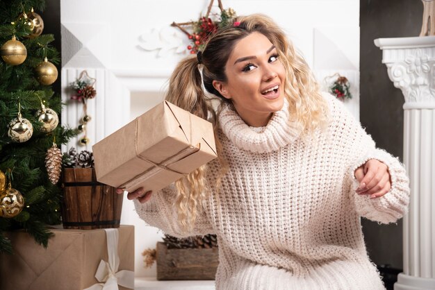 Una mujer joven con un suéter blanco que muestra dos cajas de regalos de Navidad.