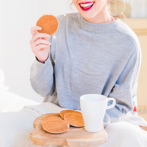 Mujer joven en suéter gris comiendo galletas