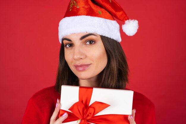 Mujer joven en un suéter de Navidad y gorro de Papá Noel con una caja de regalo