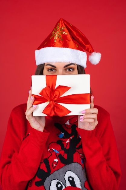 Mujer joven en un suéter de Navidad y gorro de Papá Noel con una caja de regalo