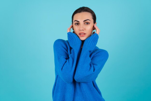 Mujer joven en suéter de punto azul y maquillaje de día natural sobre fondo turquesa