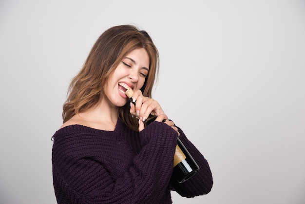 Mujer joven en suéter de punto cálido tratando de abrir una botella de vino.