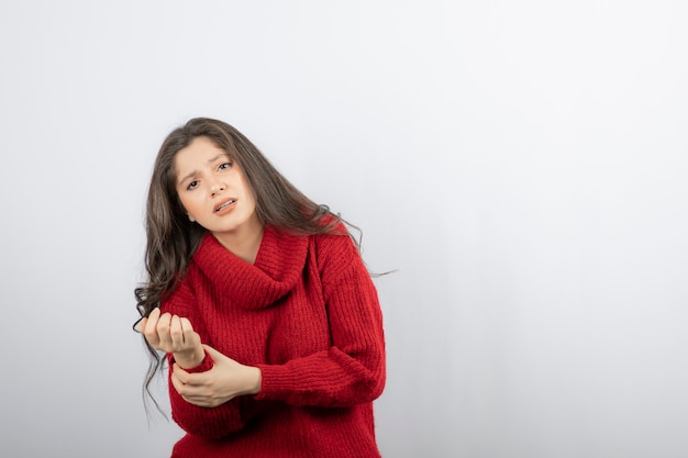 Mujer joven en suéter rojo cálido que sufre de dolor en el brazo.