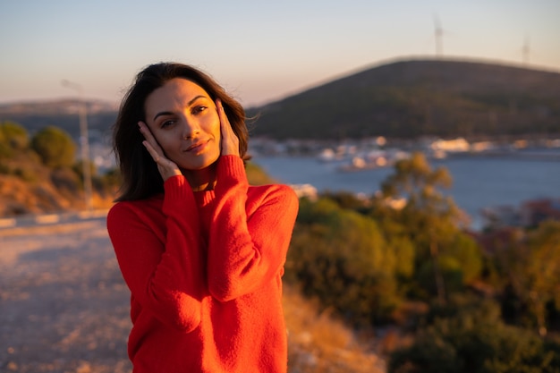 Mujer joven con un suéter rojo en una magnífica puesta de sol en la montaña