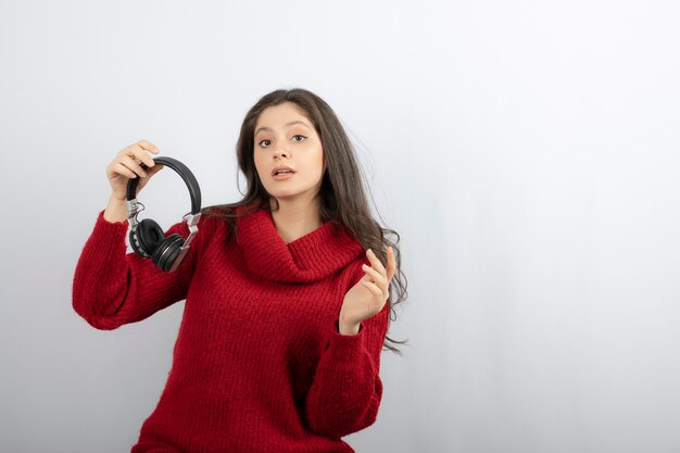 Mujer joven en suéter rojo quitándose los auriculares.