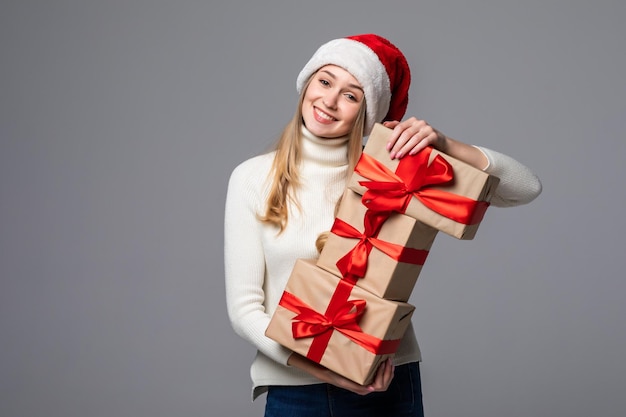 Mujer joven en suéter rojo sosteniendo cajas de regalo sobre pared gris