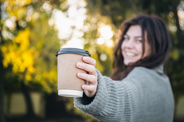 Una mujer joven en un suéter con una taza de café en la naturaleza.