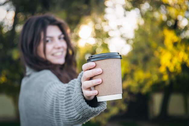 Una mujer joven en un suéter con una taza de café en la naturaleza.