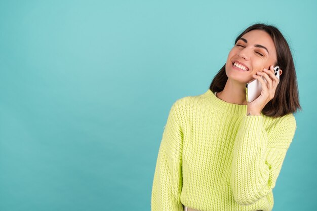 Mujer joven en suéter verde claro con teléfono móvil que tiene conversación escuchando mensaje de audio