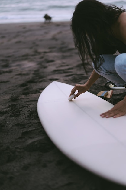 Mujer joven surfista preparando una tabla de surf en el océano encerado Mujer con tabla de surf en el océano estilo de vida activo deportes acuáticos