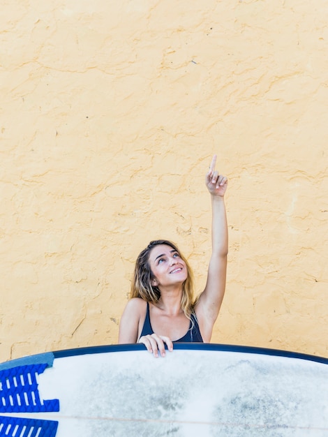 Mujer joven con tabla de surf apuntando el dedo hacia arriba