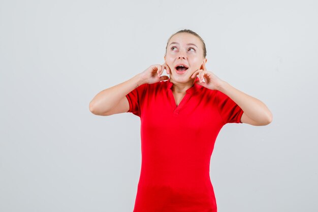 Mujer joven tapando los oídos con los dedos en camiseta roja y mirando emocionado