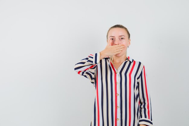 Mujer joven tapándose la boca con una blusa a rayas y mirando sorprendido