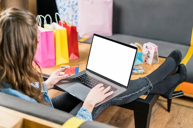 Mujer joven con tarjeta de crédito para el pago de las compras en línea en la computadora portátil