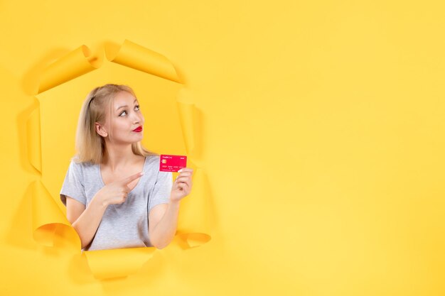 Mujer joven con tarjeta de crédito en papel amarillo rasgado fondo banco venta compras