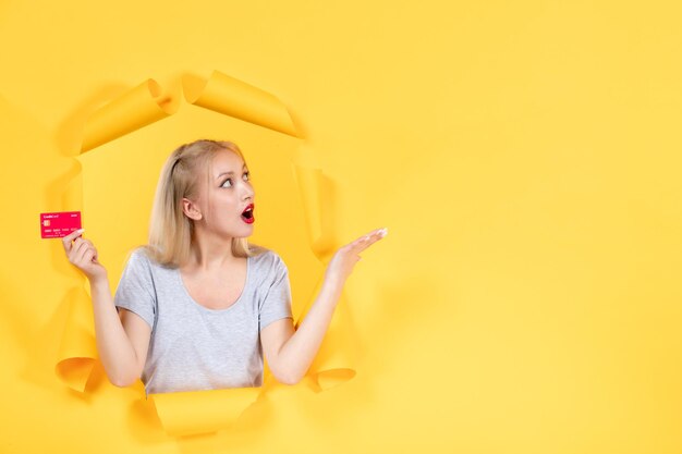 Mujer joven con tarjeta de crédito roja sobre superficie de papel amarillo rasgado