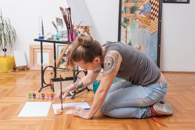 Foto gratuita mujer joven tatuada sentada en el piso y pintando