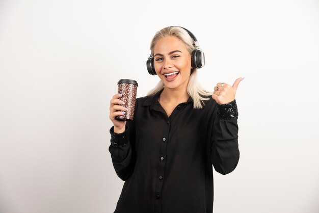 Mujer joven con taza en auriculares en una pared roja.