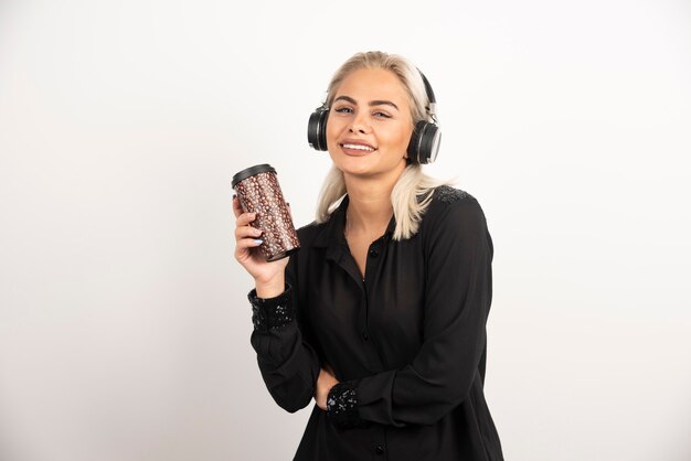 Mujer joven con taza en auriculares en una pared roja.