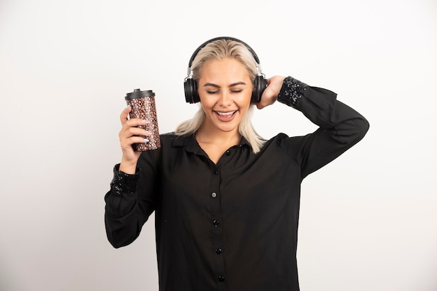 Mujer joven con taza en auriculares en una pared roja.