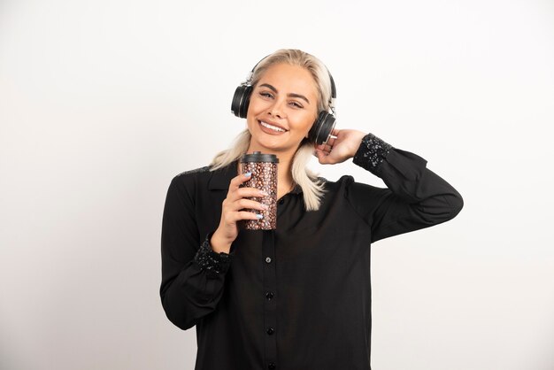 Mujer joven con taza en auriculares en una pared roja.