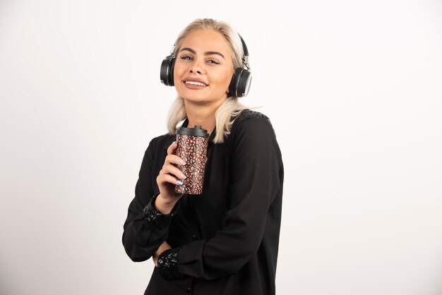 Mujer joven con taza en auriculares sobre un fondo rojo. Foto de alta calidad