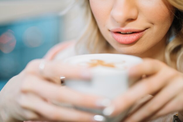 Mujer joven con taza de bebida cerca de la cara