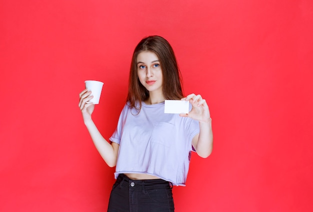 mujer joven con una taza de bebida presentando su tarjeta de visita.