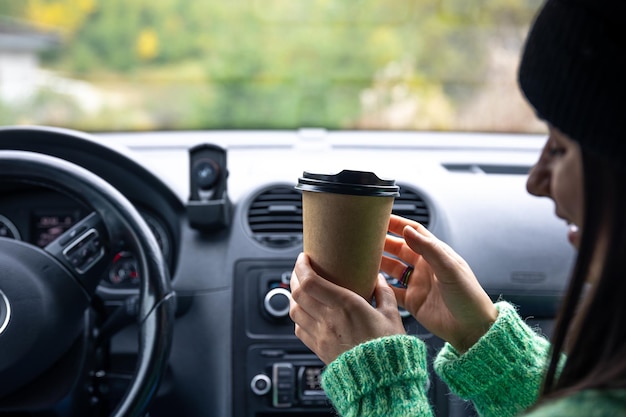 Una mujer joven con una taza de café se sienta en el concepto de viaje en coche