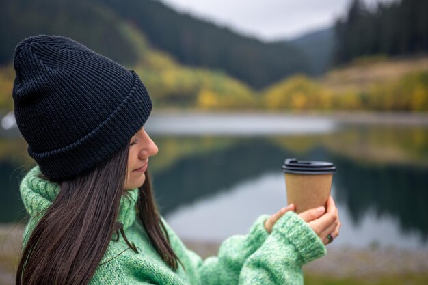 Una mujer joven con una taza de café sobre un fondo borroso de montañas