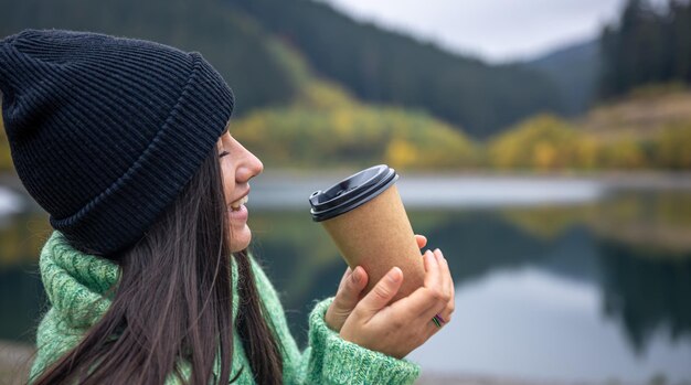 Una mujer joven con una taza de café sobre un fondo borroso de montañas