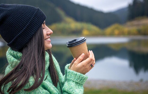 Una mujer joven con una taza de café sobre un fondo borroso de montañas