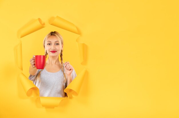 Mujer joven con una taza de té en la superficie de papel amarillo rasgado comercial publicidad facial