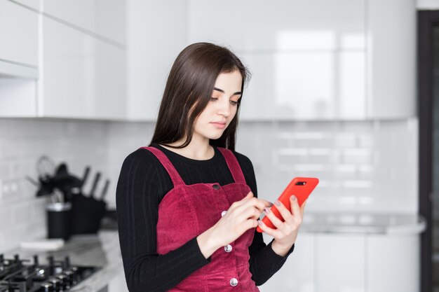 Mujer joven con teléfono celular y divertirse en la cocina