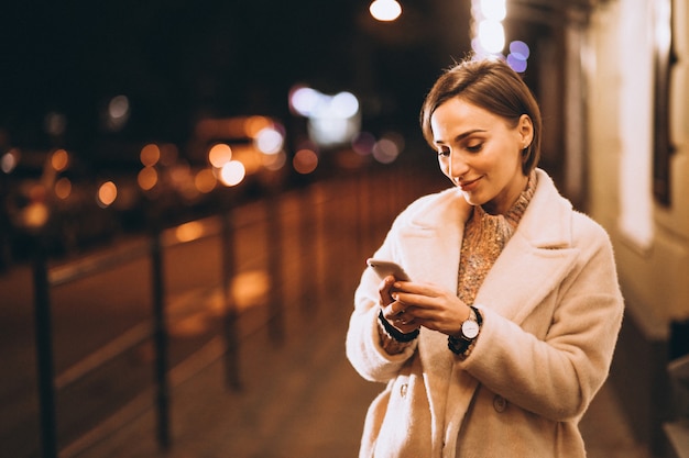 Mujer joven con teléfono fuera de la calle de noche