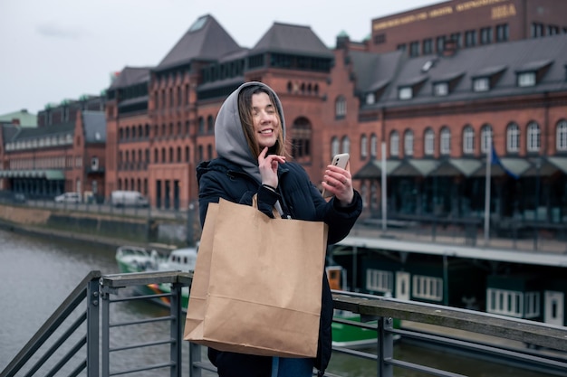 Una mujer joven con teléfono inteligente y bolsa de compras en la ciudad