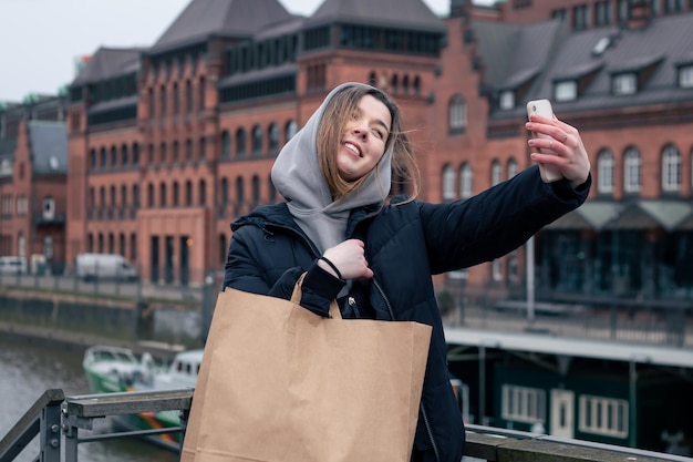 Una mujer joven con teléfono inteligente y bolsa de compras en la ciudad