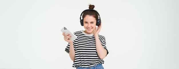 Mujer joven con teléfono inteligente escuchando música bailando su canción favorita en auriculares posando