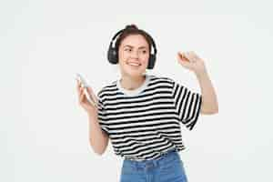 Foto gratuita mujer joven con teléfono inteligente escuchando música bailando su canción favorita en auriculares posando