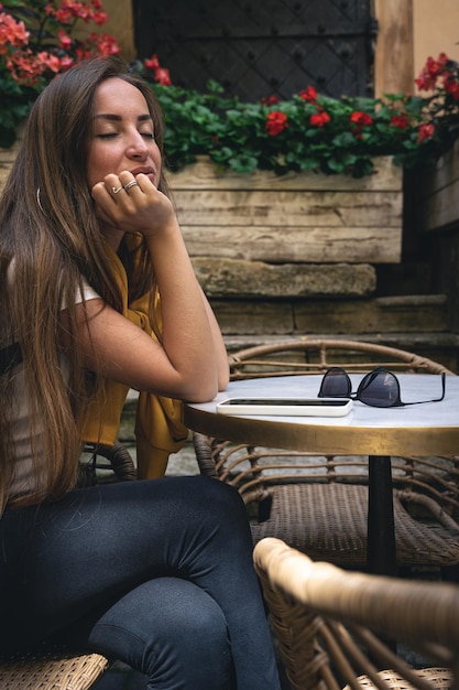 Una mujer joven con teléfono inteligente y gafas de sol en un café en la terraza