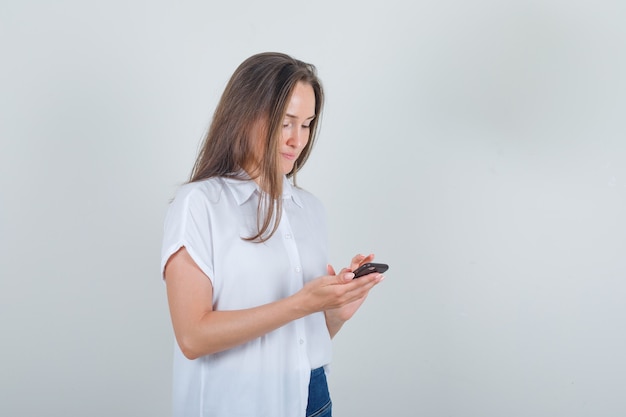 Mujer joven con teléfono móvil en camiseta, jeans y mirando ocupado